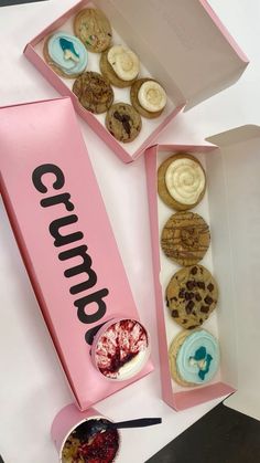 two pink boxes filled with cookies and pastries on top of a white countertop