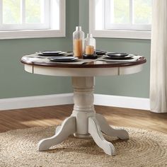 a dining table with plates on it in front of two windows and a round rug