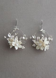 two white flowers are hanging from hoop earrings on a gray surface with beads and crystals