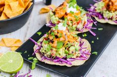 three tacos with shrimp, coleslaw and guacamole on top