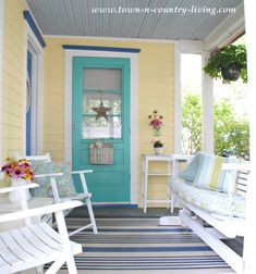 two white rocking chairs sitting on top of a porch next to a blue and yellow door