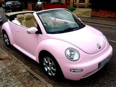 a pink convertible car is parked on the side of the road