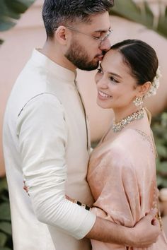 a man and woman standing next to each other with their arms around each other in front of plants