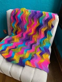 a multicolored crocheted blanket sitting on top of a white couch next to a blue wall