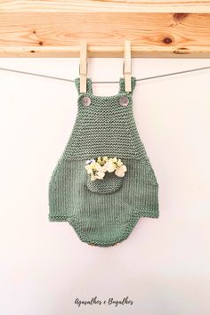 a green knitted baby's bib hanging on a clothes line with flowers in the pocket