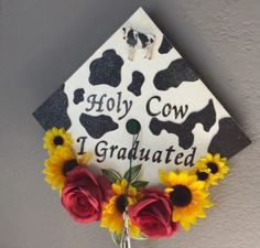 a graduation cap decorated with sunflowers, roses and cows is hanging on the wall