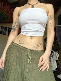 a woman with tattoos on her stomach wearing green pants