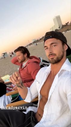 two men are sitting on the beach and one is holding something in his hand