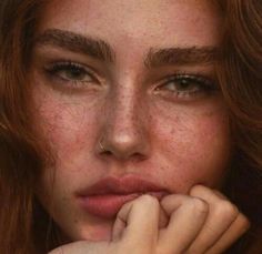 a woman with freckled hair is looking at the camera and has her hand on her face