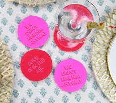 three pink and red coasters with words on them sitting next to a plate that says love is in the air