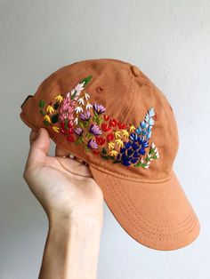 a person holding up a baseball cap with embroidered flowers on it