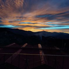 the sun is setting over some rooftops with mountains in the background