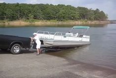 a man standing next to a truck pulling a boat out of the water on a lake