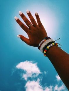 a woman's hand with white nails and bracelets on it, against a blue sky