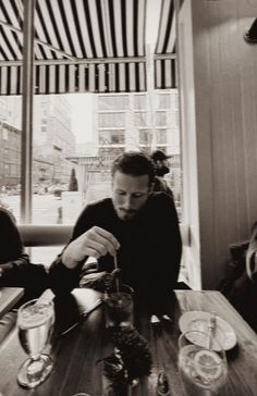 two people sitting at a table with drinks in front of them and one person holding a spoon