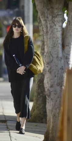 a woman is walking down the sidewalk with her hand in her pocket