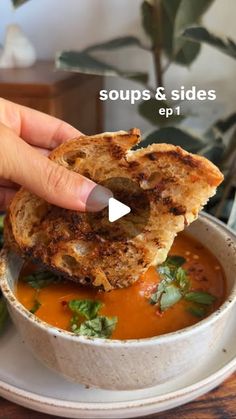 a person dipping some food into a bowl with soup and bread on the side,