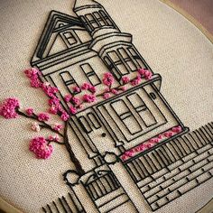 a close up of a embroidery on a piece of cloth with pink flowers in front of a building