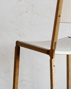 a white chair with wooden legs and a seat cushion on top of it, against a white wall