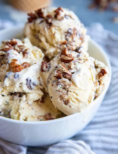 three scoops of ice cream in a white bowl with pecans and walnuts