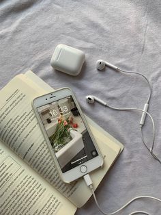 an open book, headphones and cell phone on a bed