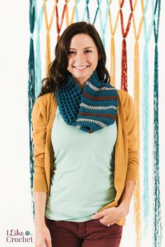 a woman standing in front of a multicolored crocheted scarf and smiling