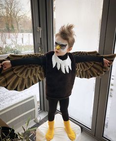 a young boy dressed up as an eagle with his wings spread out, standing in front of a window