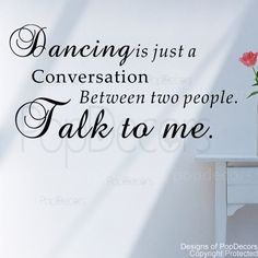 a vase with flowers sitting on top of a table next to a wall that says dancing is just a conversation between two people talk to me