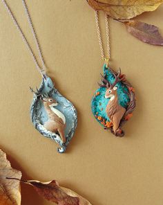 two necklaces with animals on them sitting next to leaves