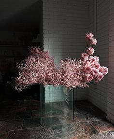 some pink flowers are in a vase on the floor near a brick wall and window