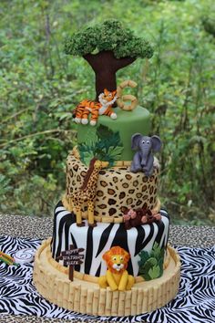 a tiered cake decorated with animals and zebras is on a table in front of trees