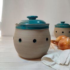 two ceramic containers with faces on them sitting on a table next to onions and garlic