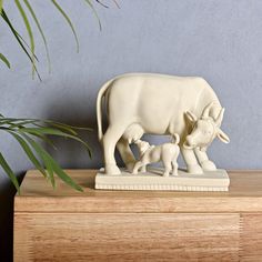 a white cow and calf figurine sitting on top of a wooden table next to a potted plant