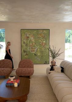 a woman is standing in the living room with her dog and large painting on the wall