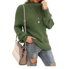 a woman wearing a green sweater and ripped jeans is talking on her cell phone while holding a handbag