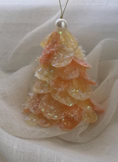 a glass christmas tree ornament hanging on a white cloth with a pearl bead