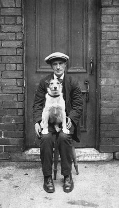 an old black and white photo of a man holding a dog