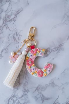 the letter c is decorated with flowers and tassels on a keychain