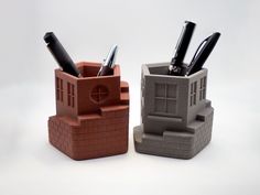 two pen holders made out of clay with pens and pencils in them on a white surface