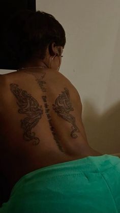 the back of a woman with tattoos on her upper and lower back, sitting in bed