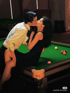 a man and woman kissing on top of a pool table