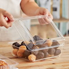 a person holding a plastic container filled with donuts on top of a wooden table