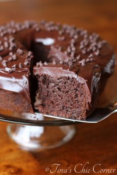 a chocolate cake on a glass plate with one slice cut out and ready to be eaten