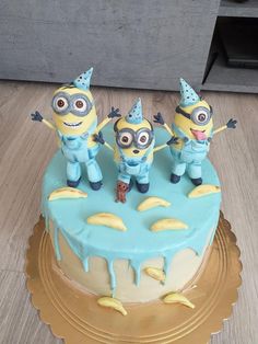 three minion figurines on top of a blue and yellow cake covered in frosting