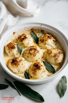 a white bowl filled with dumplings covered in cheese and sage leaf garnish