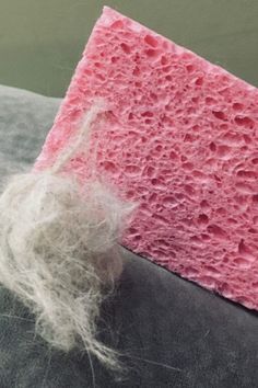 a piece of pink and white sponge sitting on top of a gray surface next to a wool ball