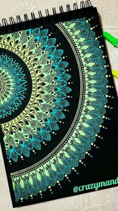 a spiral notebook with green and blue designs on it next to crayon markers