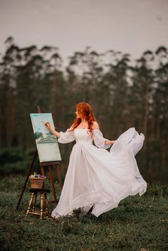 a woman in white dress standing next to an easel