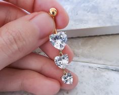 a person holding an earring with three heart shaped diamonds on it's side