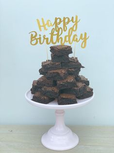 a birthday cake made out of brownies on top of a white plate with a gold happy birthday sign